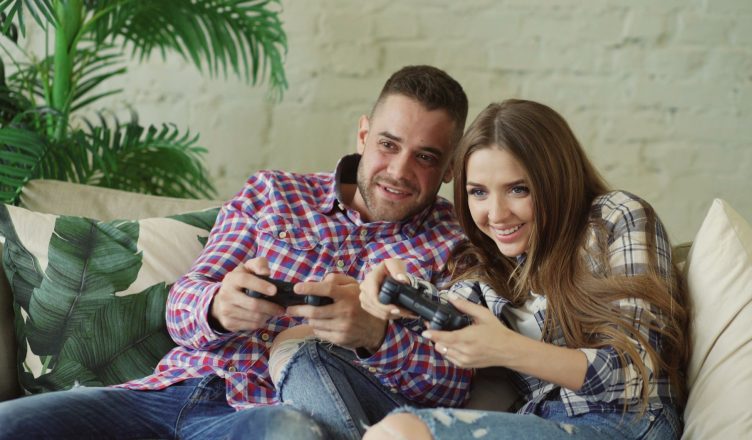 Happy couple enjoying video games together at home on a cozy sofa. — Take Advantage of Welcome Bonus Offers and Other Promoti