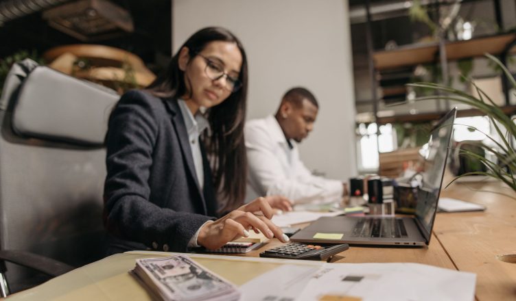 Two business professionals collaborating with a laptop and calculator in a modern office. — Tax Return and Your Choices