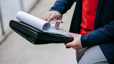 Close-up of a professional person reviewing documents outdoors. Engaged in work with focus on writing materials. — Technologi