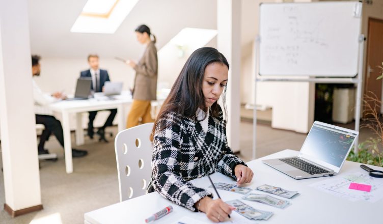 Focused businesswoman reviewing financial documents and currency in a modern office setting. — The rise of cryptocurrency tra
