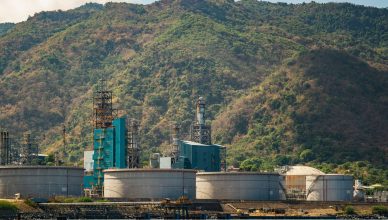 Industrial plant with large tanks and chimneys against a lush mountain backdrop. — The Role of a Good Welder in a Constructio