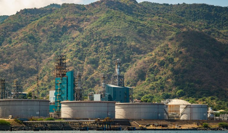 Industrial plant with large tanks and chimneys against a lush mountain backdrop. — The Role of a Good Welder in a Constructio