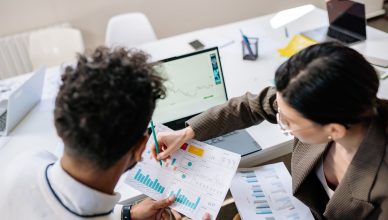 Two colleagues in a meeting room discussing financial charts and graphs on a laptop and paper. — Universal Asset Management T