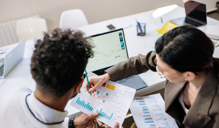 Two colleagues in a meeting room discussing financial charts and graphs on a laptop and paper. — Universal Asset Management T