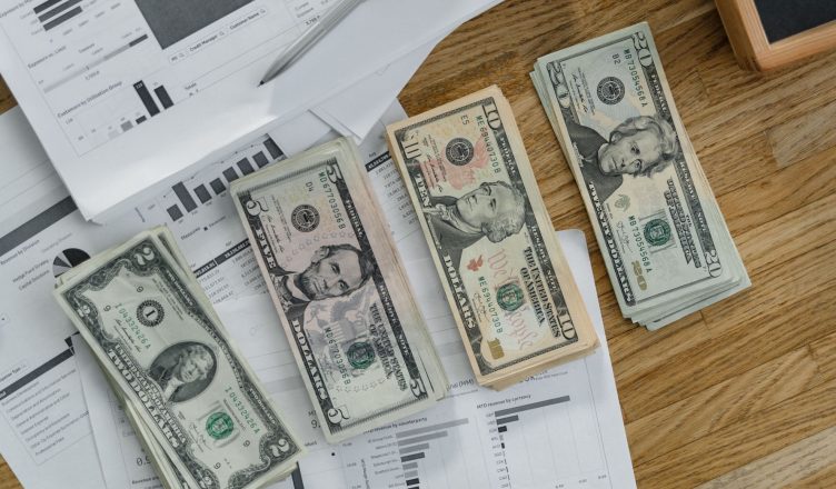 Stacks of US Dollar banknotes placed over financial documents and reports on a desk. — Various Home Loan Fees and Charges Tha