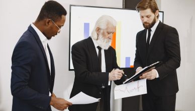 Three businessmen in suits reviewing reports and graphs during an office meeting. — Various uses of deploy core banking and f