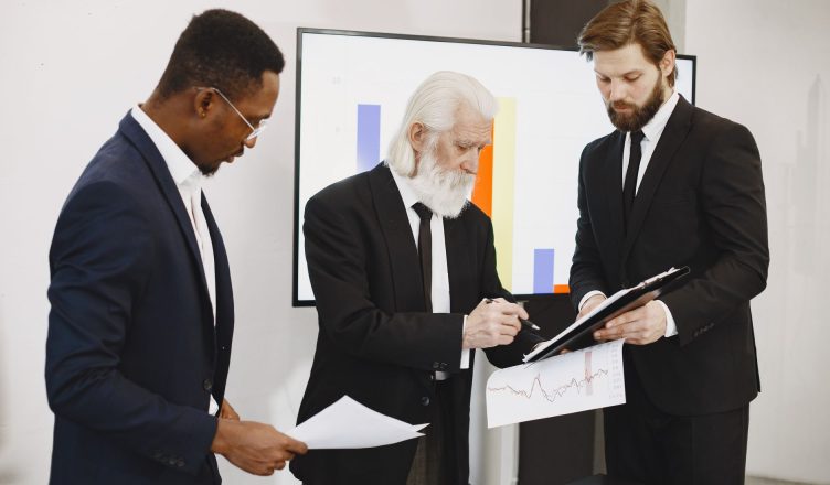 Three businessmen in suits reviewing reports and graphs during an office meeting. — Various uses of deploy core banking and f