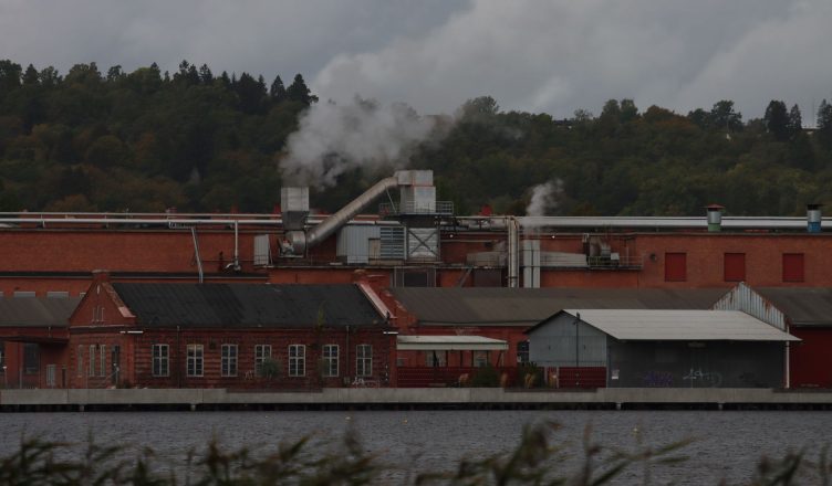 A factory with smoke emitting from chimneys along a river, surrounded by trees. — What Can I Do With a Belt Alignment Tool?
