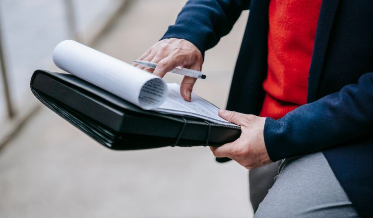 Close-up of a professional person reviewing documents outdoors. Engaged in work with focus on writing materials. — Which Indi