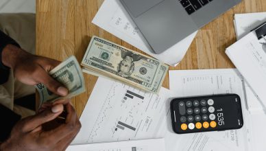 Close-up of hands counting cash on desk with calculator, charts, and laptop — Which Type of Life Insurance Plan Suits You the