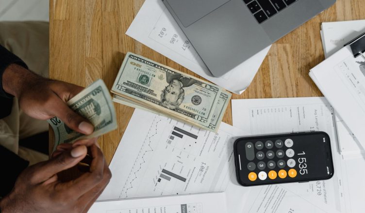 Close-up of hands counting cash on desk with calculator, charts, and laptop — Which Type of Life Insurance Plan Suits You the