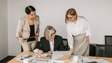 Three businesswomen discussing documents during a meeting in a modern office setting. — Why Adult Product Stores are a Boon f