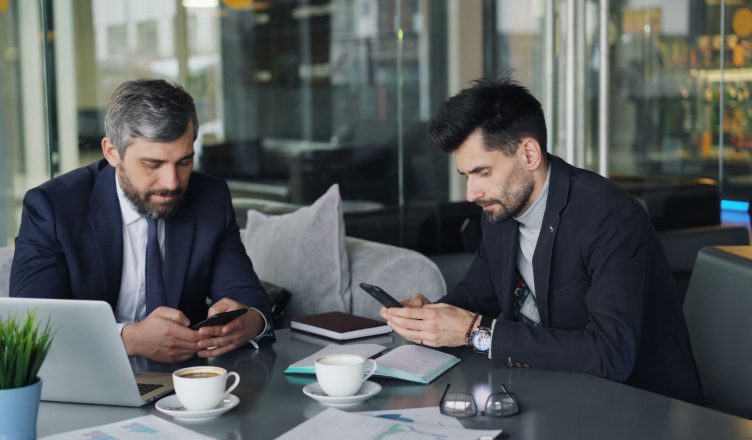 Two businessmen in a cafe working on smartphones and laptops, engaged in a meeting. — Why is the logo a must for branding obj